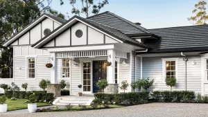 Front view of light gray Tudor-style house with dark tile roof, white trim, porch, and manicured garden